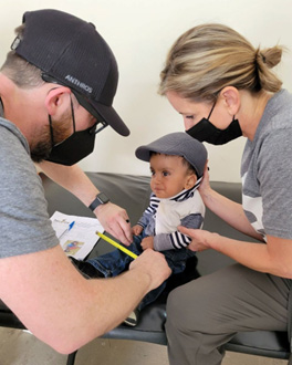 Two people with medical masks giving a small child a medical examination.