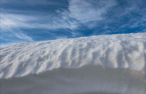 A large snowdrift is set against a blue sky with a few scattered clouds.